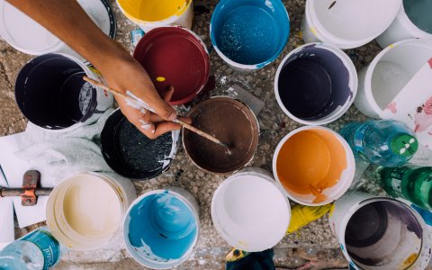 An overhead view of a person dipping a paintbrush into a pot of paint.